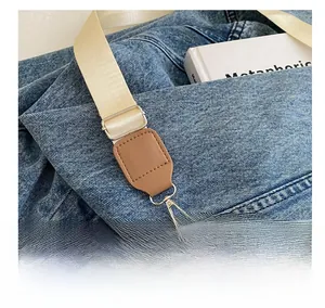 Detail of silver hardware hook and adjustable woven strap on blue denim crossbody bag