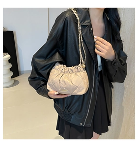 Dettaglio della borsa a secchiello beige trapuntata con catena dorata e metallo
