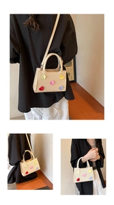Detailed close-up of woven beige crossbody bag featuring 3D colorful heart patches