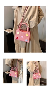 Close-up of pink woven handbag with colorful 3D heart patches and dual-purpose straps