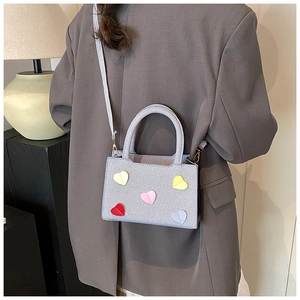 Detail of grey crossbody bag with colorful heart patches on premium twill fabric texture