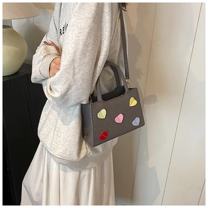 Detail showing grey textured crossbody bag with colorful heart patches on female model