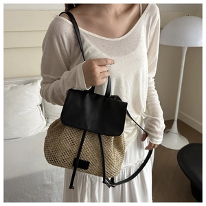 Detail of straw woven backpack with black leather straps worn by a model in a minimal room
