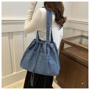 Detail of blue denim tote bag featuring dual front pockets and drawstring closure