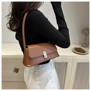 Elegant brown faux leather underarm bag with gold clasp shown on a model in a modern room