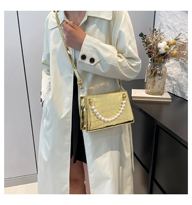 Detailed close-up of metallic gold crocodile pattern handbag with pearl chain decoration