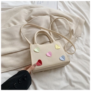 Détail du sac bandoulière beige tissé orné de cinq patchs cœurs colorés sur le devant