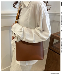 Detailed view of brown leather crossbody bag with wide strap and gold hardware on model