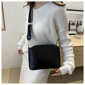 Detail of vintage black leather shoulder bag with wide contrast strap on white sweater