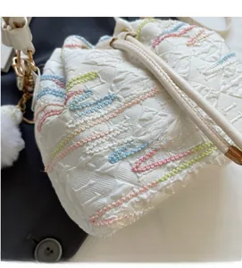 Close-up of white drawstring bucket bag with colorful wavy embroidery and plush charm