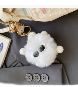 Close-up of fluffy white plush charm with metal keychain on a rainbow striped bag
