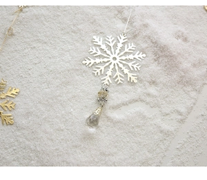Detail of golden metal snowflake ornament with faux crystal drop on snowy background