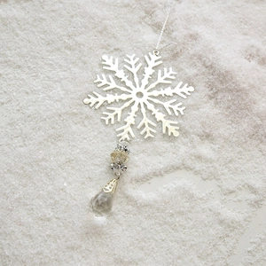 Metal snowflake ornament with crystal pendant on white snow background for Christmas decor
