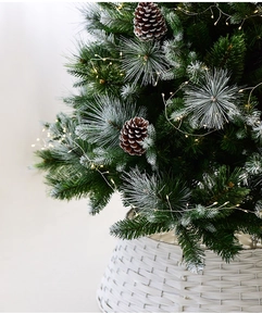 Detail of snow-flocked Christmas tree with pine cones, LED lights and white woven basket