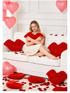 Close-up of soft red lip-shaped plush pillows in a romantic setting with rose petals