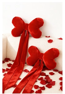 Detail of red velvet bow pillows with ribbons and rose petals on a white sofa