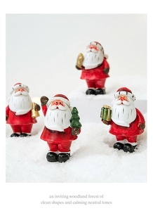 Miniature Santa Claus figurines with holiday decor on a snowy white background