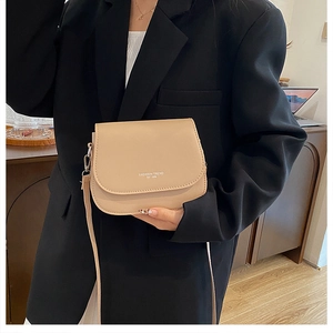 Detail of a beige saddle bag with fashion trend lettering worn with a black blazer