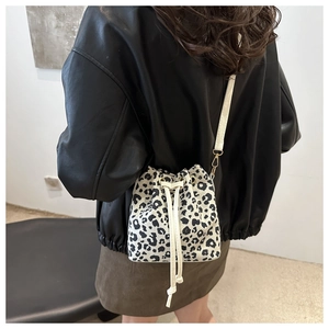 Chic leopard print bucket bag with white drawstring shown as a crossbody on a model