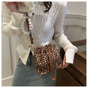 Detail of leopard print bucket bag with drawstring closure and white bead charm on a model