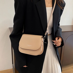 Minimalist beige saddle bag with adjustable strap worn by a model in a modern outfit