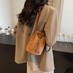 Brown suede bucket bag with drawstring closure worn by model in a cafe setting