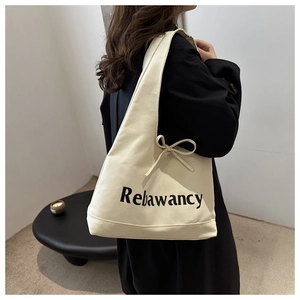 Detail of off-white canvas tote bag featuring black lettering and side bow decoration