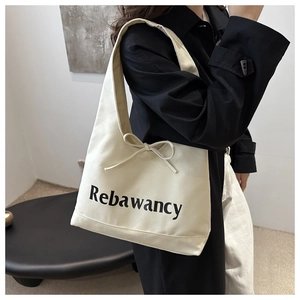 Close-up of cream canvas tote bag featuring black lettering and a delicate bow detail