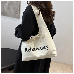 Detail of minimalist cream canvas tote bag with Rebawancy text and ribbon bow accent