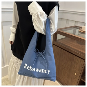 Detail of blue canvas tote bag featuring white logo text and a delicate bow tie decoration