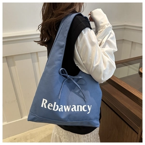 Blue canvas tote bag with Rebawancy text and side drawstring bow detail on model
