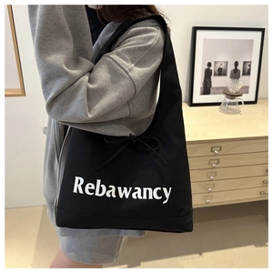 Detail of black canvas tote bag with white Rebawancy text and decorative ribbon