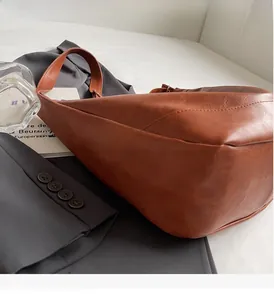 Detail of soft brown leather hobo bag texture and curved stitching on a grey suit jacket