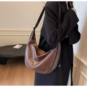 Detail of deep brown soft leather tote bag worn with a black coat in a minimalist setting