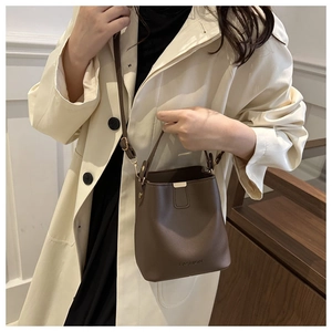 Borsa a secchiello marrone con logo FASHION indossata con un elegante trench beige