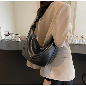 Close-up of black pleated hobo bag with wide shoulder strap worn by a model in a cafe