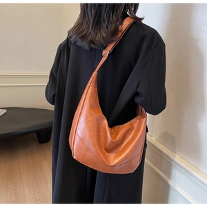 Brown moon-shaped hobo bag in soft textured leather worn over a black coat