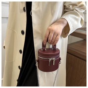 Detail of dark red mini cylindrical crossbody bag with white stitching and silver chain