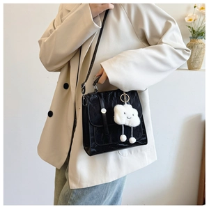 Detail van zwarte crossbodytas met crinkle-effect en witte pluche wolkenhanger eraan