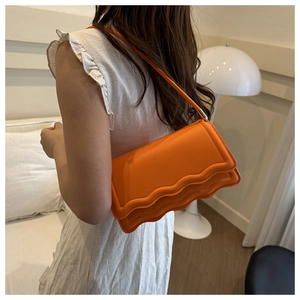 Dettaglio di una borsa baguette in pelle arancione vivace con bordo ondulato unico