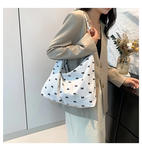 Detail view of a white canvas tote bag with black bow print on a model in a beige blazer