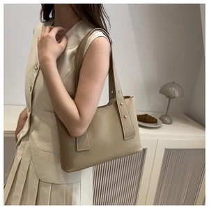 Detail der beigen Eimer-Tasche mit Metallnieten und glatter Ledertextur im minimalistischen Stil