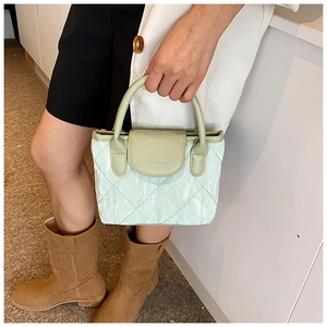 Detail of mint green quilted handbag featuring a silver fashion logo and arched handles