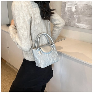 Detail of silver quilted bucket bag with metallic finish and top handle on a beige knit sweater