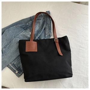 Black canvas tote bag detail with brown leather handles and adjustable metal buckle