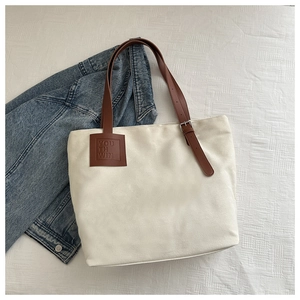 Detail of canvas tote bag featuring brown leather straps and a vintage brand patch
