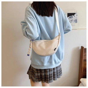 Detail of a cream half-moon canvas crossbody bag worn by a model in a casual setting