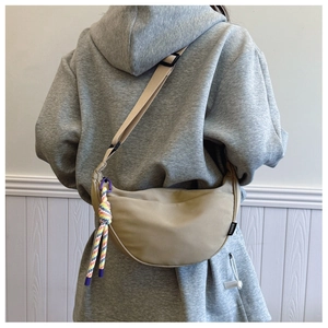 Detail of khaki crescent crossbody bag with woven strap and colorful rope accessory