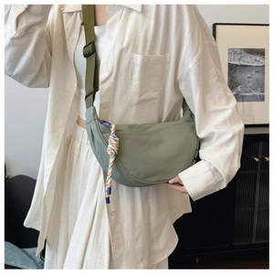 Detail of light green crescent nylon bag with adjustable strap and braided charm accent
