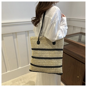 Detail of woven straw tote bag featuring black stripes and thin leather shoulder straps